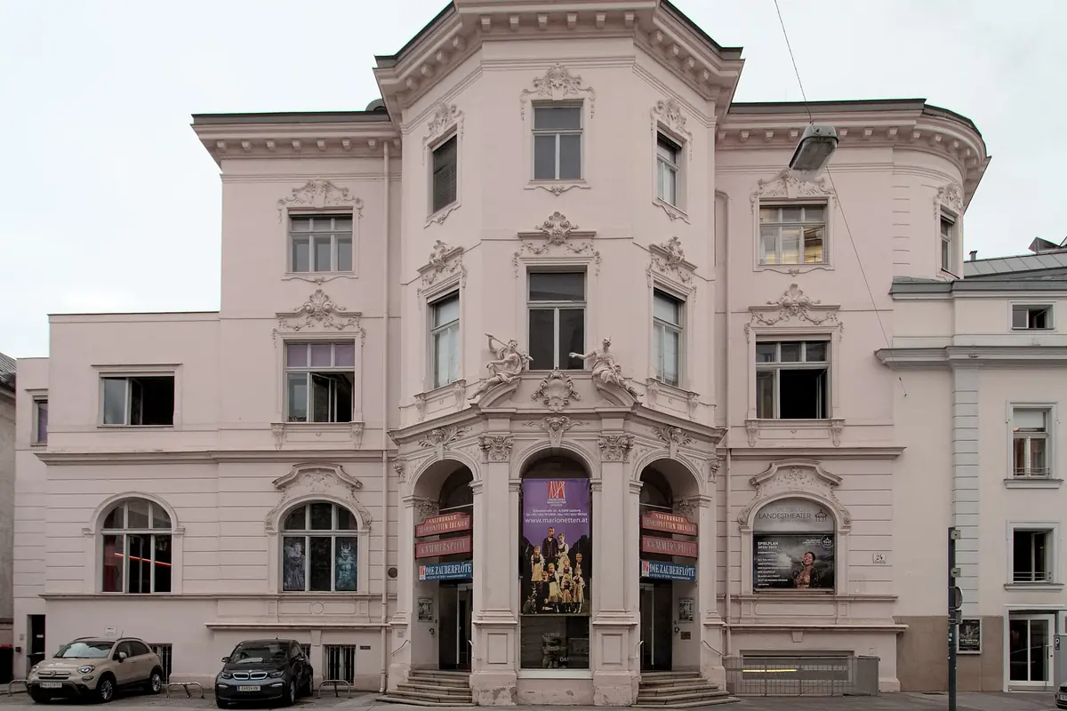 Den lyseblommerøde barokfacade på teaterbygningen på Schwarzstraße med tre buede indgangsdøre og mansardtag
