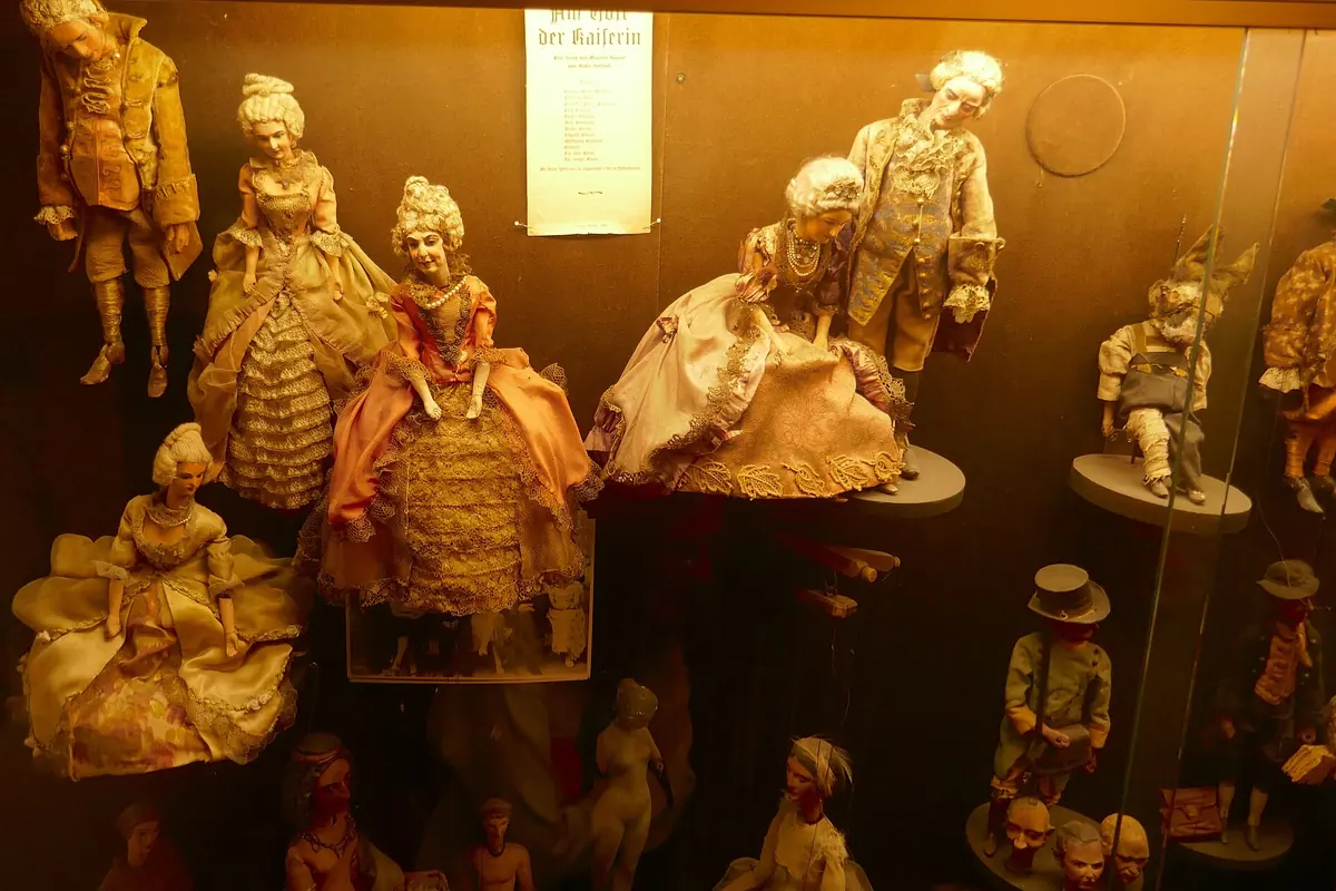 Marionetter i attenhundredetalsdragter med pudret hår og fyldige skørter står inde i en oplyst montre